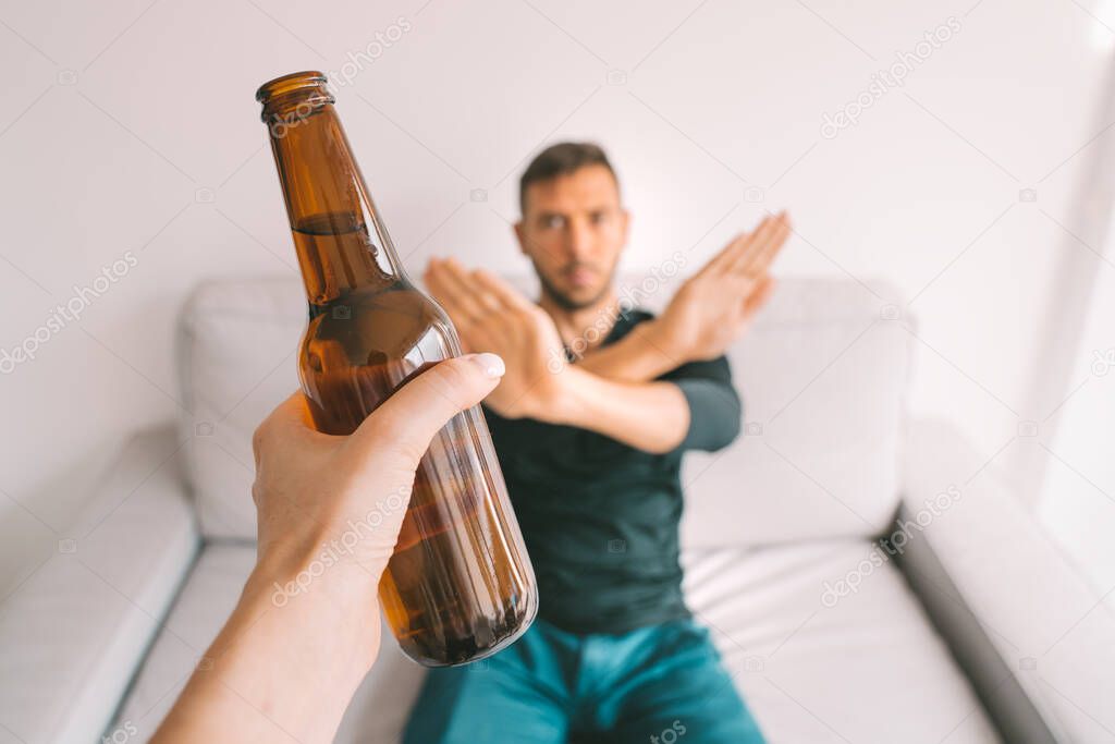 No alcohol. Stop alcoholism. Young man refusing to drink beer, showing showing rejection sign to bottle of beer