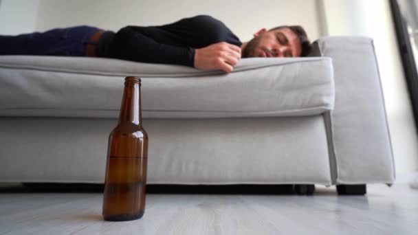 Részeg fiatalember egy üveg sörrel a kanapén alszik otthon.. — Stock videók