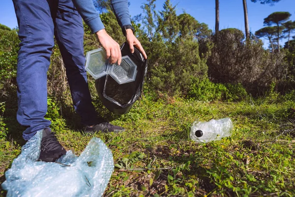 Man cleaning-up the forest of plastic garbage. Nature cleaning. Volunteer picking up a plastic in the woods. Outdoor trash and rubbish. Green and clean nature. Plastic awareness activism and ecology.