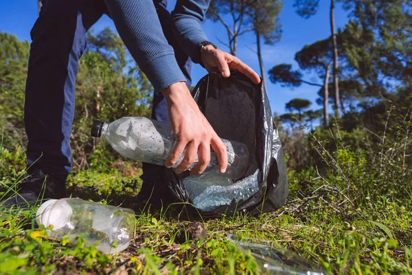 Man cleaning-up the forest of plastic garbage. Nature cleaning. Volunteer picking up a plastic in the woods. Green and clean nature. Planet care and ecology concept