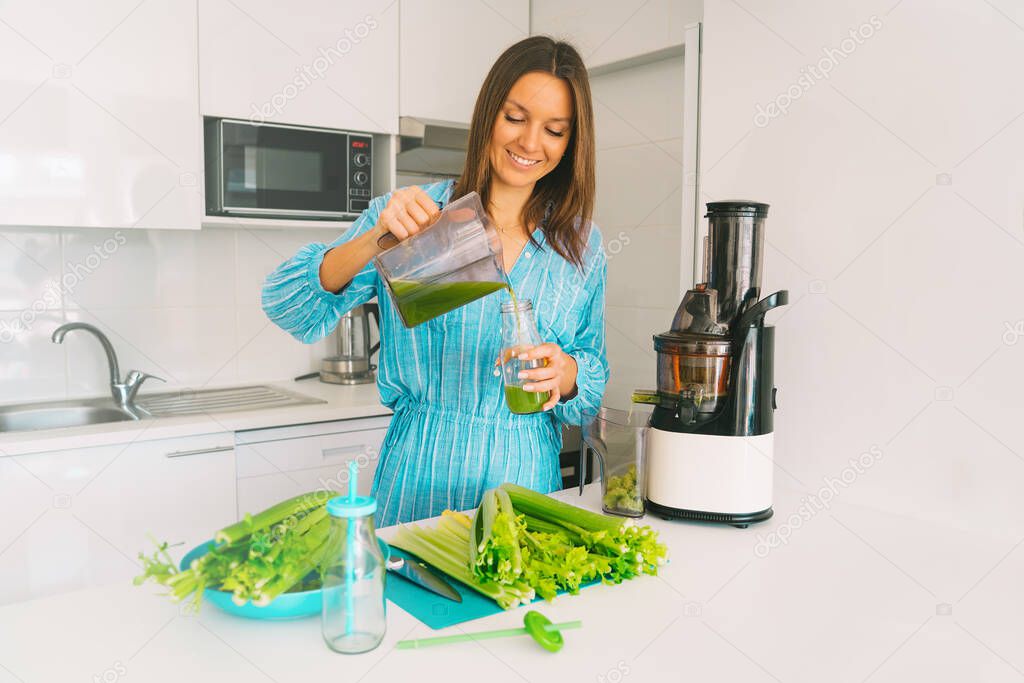 Fresh homemade celery detox juice. Healthy young woman making freshly pressed celery juice in juicer machine at home. Healthy detox diet