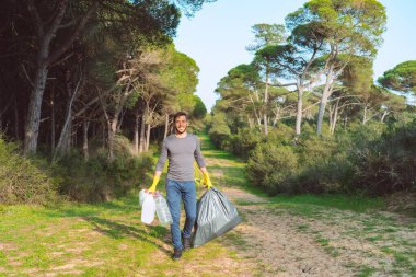 Ormanda çöp toplama. Çöp torbasıyla gönüllü adam, plastik kirlilikten ormanı temizliyor. Doğadaki çöpleri topluyorum. Çevre koruma kavramı. Halk ve ekoloji