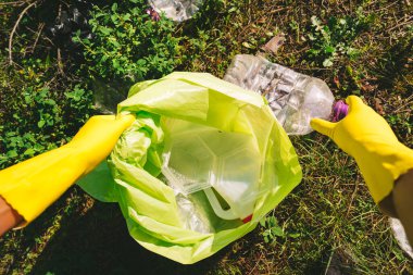 Sarı koruyucu eldivenli gönüllü parktaki çöp torbasında çöp topluyor. Doğadaki çöpleri topluyorum. Çevre koruma kavramı. Halk ve ekoloji