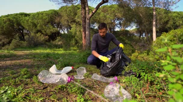 Voluntario con guantes protectores amarillos recogiendo basura en la bolsa de basura en el bosque. Recogiendo basura en la naturaleza. Concepto de protección ambiental. Personas y ecología — Vídeos de Stock