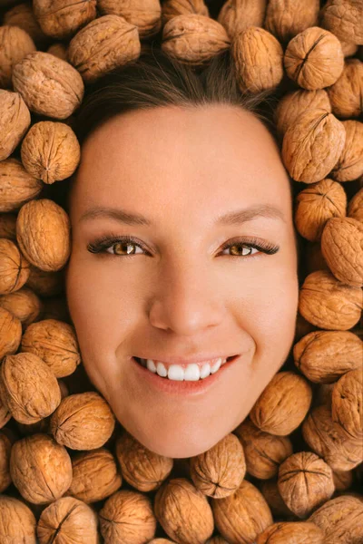 Cara sonriente de mujer sobre fondo de nueces. Comiendo nueces. Dientes fuertes —  Fotos de Stock