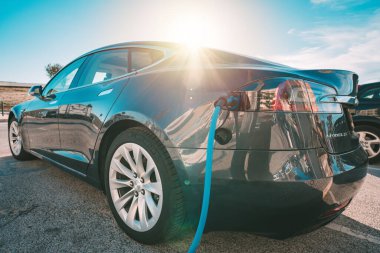 Otoparkta şarj edilmiş Tesla elektrikli arabası ya da EV arabası. Güç kablosu fişe takıldı. Çevre dostu alternatif enerji. 18.03.2021, Casta Da Caparica, Portekiz