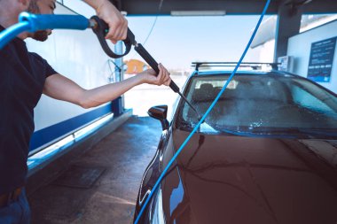 Adam oto yıkamada araba yıkıyor. Yüksek basınçlı su kullanarak arabayı temizlemek. Araba yıkama.