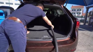 Genç adam oto yıkama istasyonunda elektrikli süpürgeyle araba temizliyor.