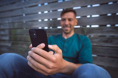 Man having a facetime video call with his black modern smartphone outdoors. Looking at smartphone