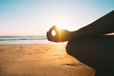 Meditating on the beach at sunrise in the morning. Sitting on the sand in easy pose or sukhasana with gyan mudra. Relaxation and harmony with nature