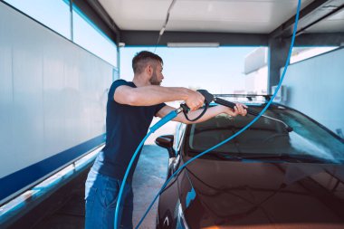 Young man washing car in self serve car wash. Cleaning car using high pressure water. Car smart wash
