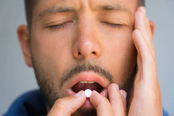 Man suffering from headache. Painkillers to relieve pain. Close up of man face holding temple and taking pill because of strong headache. Medicine or tablet from migraine, tension or cluster headache