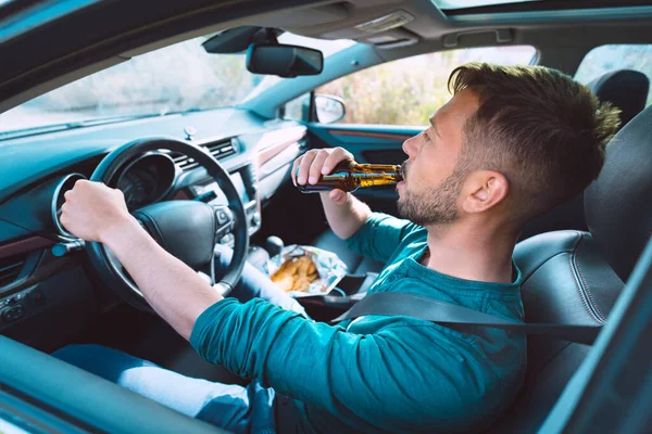 Dronken rijdend. Jongeman die bier drinkt terwijl hij in een auto rijdt. Bestuurder onder invloed van alcohol. Het begrip "gevaarlijk rijden". — Stockfoto