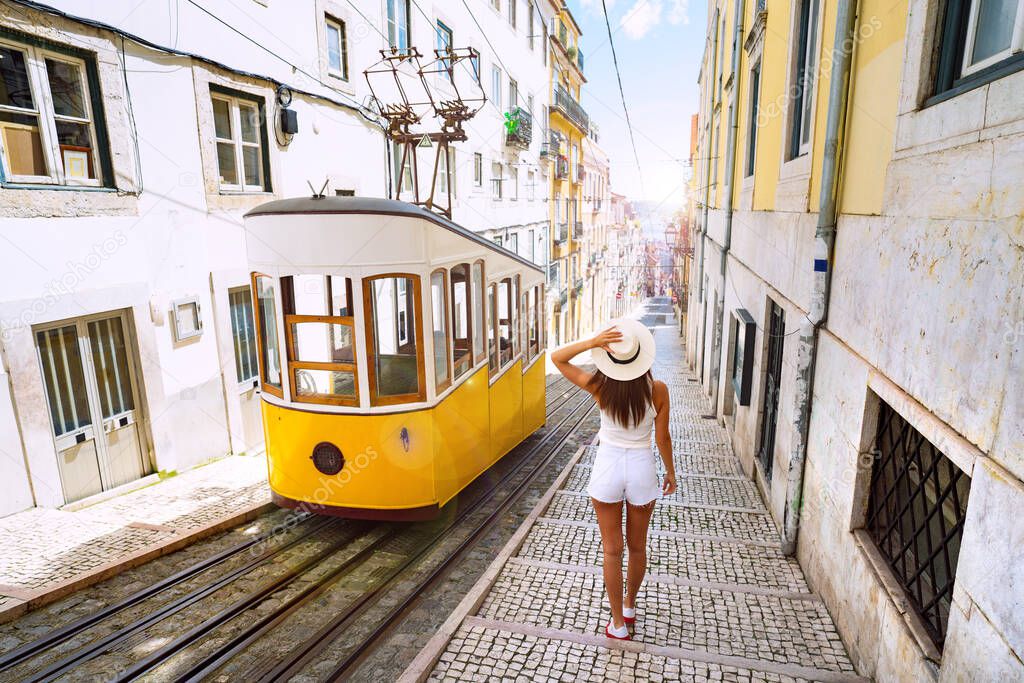 Woman tourist walking in narrow streets of Lisbon city old town. Famous retro yellow funicular tram on a sunny summer day. Tourist attraction. Vacation and travel concept.