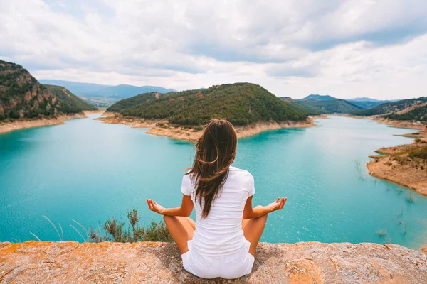Giovane donna sana in abiti bianchi meditare o praticare yoga nella natura. Donna seduta in posizione yoga, posa facile o sukhasana con mudra con bella vista sul lago blu. Relax, armonia. — Foto Stock