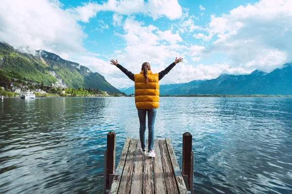 Giovane viaggiatrice a braccia aperte in piedi su un ponte di legno e gode di una splendida vista sul lago di Ginevra in Svizzera — Foto Stock