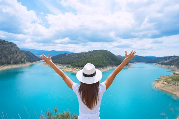 Giovane turista donna in abiti bianchi e cappello da sole a braccia aperte godersi la natura e una splendida vista sul lago con acqua pura blu in Spagna. Viaggio, buona vita e libertà — Foto Stock