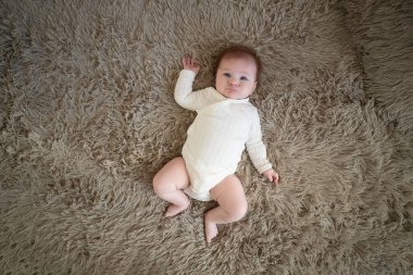 Beyaz elbiseli tatlı bir kız bebek yatakta emekliyor. Sevimli çocuk portresi. 3 aylık çocuk. Yüksek kalite fotoğraf