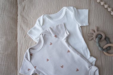 Beyaz bebek kıyafetleri, aksesuarlar ve kahverengi arka planda oyuncaklar. Yeni doğmuş vücut giysisi ve eldivenler. Bebek gereksinimleri ve annelik kavramı. Yüksek kalite fotoğraf
