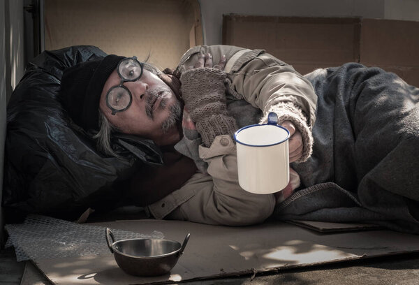 A homeless man receives a facemask from a passer-by as he is jobless and hungry. He lives by the sidewalk due to the covid 19 pandemics.
