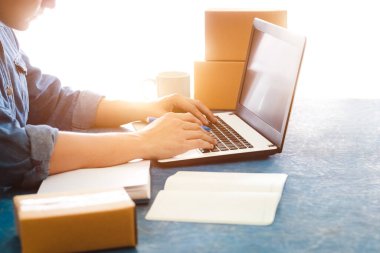 Genç Asyalı erkekler dizüstü bilgisayarlarla müşterilerden yeni siparişler alıyor, ev sahibi arka planda çalışıyor, çevrimiçi alışveriş e-ticareti veya serbest çalışma konsepti üzerinde çalışıyor.