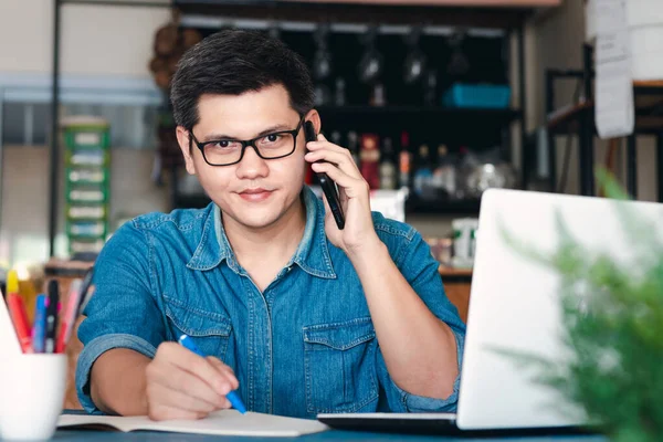 Young Asian men answer the phone happy after new order from customer, business owner working at home office packaging on background, online shopping e-commerce or freelance working concept.