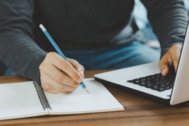 Genç adam ders çalışırken çalışma masasında oturup laptopta webinar podcast izleyerek eğitim konferansı ve e-öğrenim konsepti dinliyor..