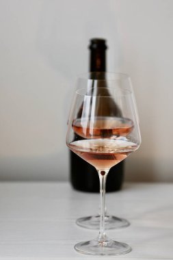 Bir kadeh kırmızı şarap ve beyaz bir iç mekanda bir şişe siyah şarap.