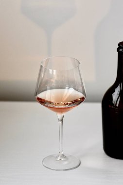 Bir kadeh kırmızı şarap ve beyaz bir iç mekanda bir şişe siyah şarap.