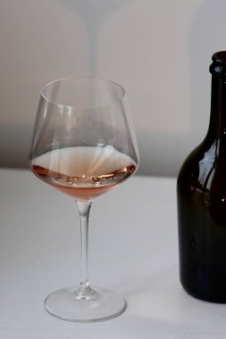 Bir kadeh kırmızı şarap ve beyaz bir iç mekanda bir şişe siyah şarap.