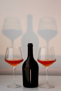 Bir kadeh kırmızı şarap ve beyaz bir iç mekanda bir şişe siyah şarap.
