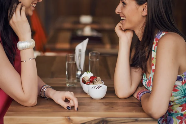 Dos chicas en una cafetería, sonriendo, cotilleando, bebiendo café — Foto de Stock