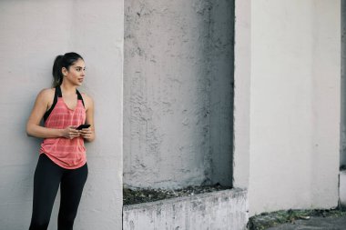 Çekici sporcu kadın duvara yaslanıyor ve uzun koşuda akıllı telefon kullanıyor..