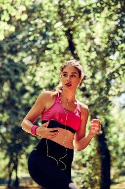 Çekici bayan koşucu doğada koşuyor ve akıllı telefondan müzik dinliyor..