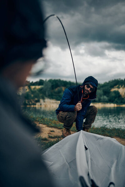 Two men adjusting tent on camping trip.