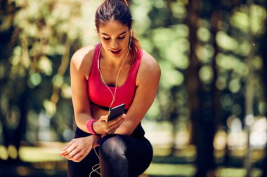 Gülümseyen sporcu kadın çömeldi, mola verdi ve doğada koştuktan sonra telefonu kullandı..