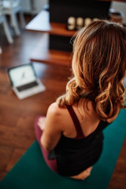 Orta yaşlı bir kadın yoga yapıyor, Corona virüsü salgını sırasında dizüstü bilgisayarındaki bir dersi takip ediyor..