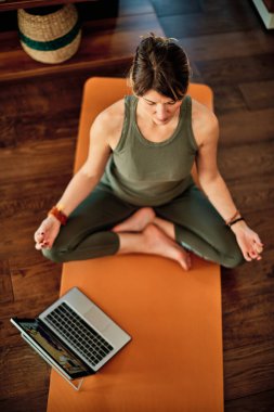 Orta yaşlı esmer, Lotus 'ta poz verip evde meditasyon yaparken video derslerini takip ediyor..
