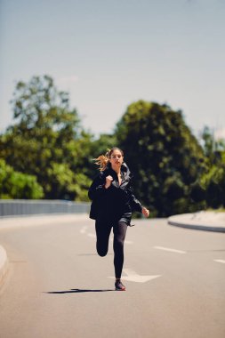 Güneşli bir günde yolda koşan hızlı sporcu kadın..