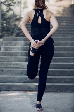 Zinde kadın koşucunun merdivenlerde ayakta dikilirken bacağını esnetiş görüntüsü..