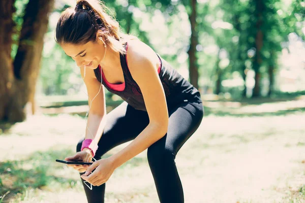 Una Corredora Sonriente Apoyada Las Rodillas Tomando Descanso Usando Teléfono — Foto de Stock