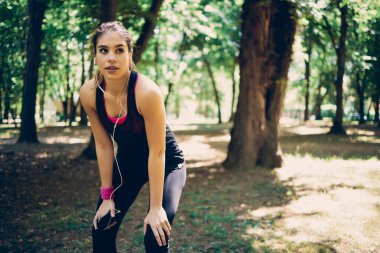 Genç, çekici, fit, beyaz tenli sporcu kadın doğada duruyor ve akıllı telefonu kullanarak koşmak için müzik arıyor..