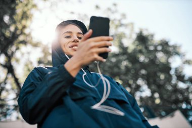 Başında kapüşonlu, gülümseyen kadın koşucu telefonla bekliyor..