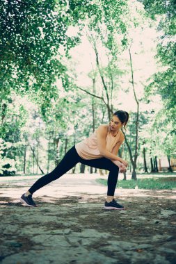 Bacaklarını esneten ve doğada ısınma egzersizleri yapan bir sporcu kadın..