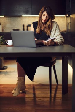 Evde oturup ilginç bir kitap okuyan hamile bir kadın. Masada bir dizüstü bilgisayar var..