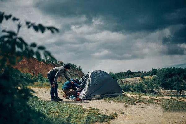 Two men on a camping trip in the nature putting backpack in a tent.
