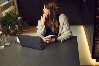 Çekici hamile esmer kadın yemek masasında oturup kitap okuyor..