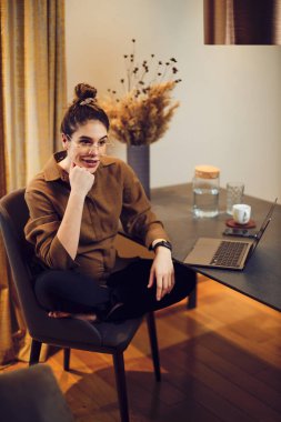 Evde yemek masasında oturan ve karantina sırasında işe ara veren hamile bir serbest çalışan..