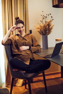 Evde yemek masasında oturan ve karantina sırasında işe ara veren hamile bir serbest çalışan..