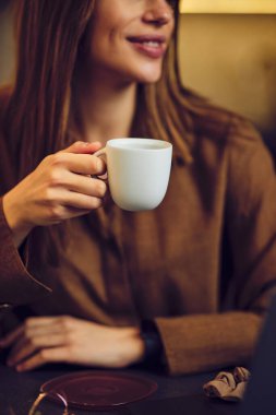 Masada oturan ve sabah kahvesinin tadını çıkaran kadının yakın plan fotoğrafı..